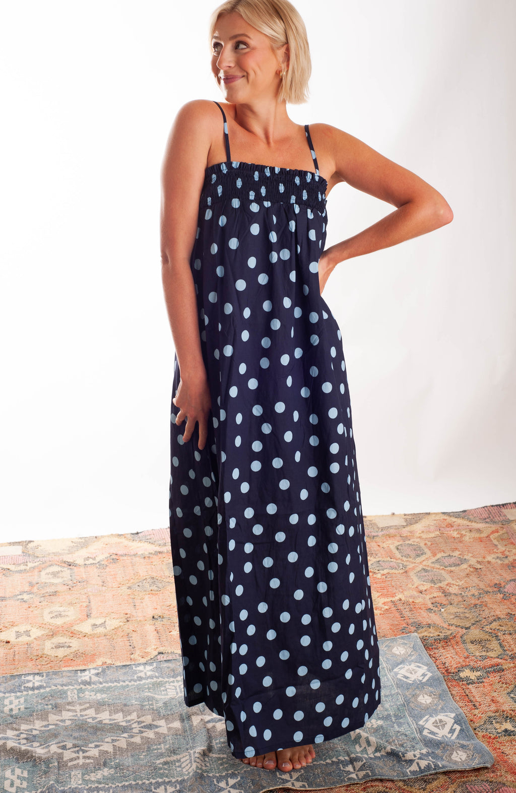 Women wearing a blue polka dot dress against a neutral backgorund.