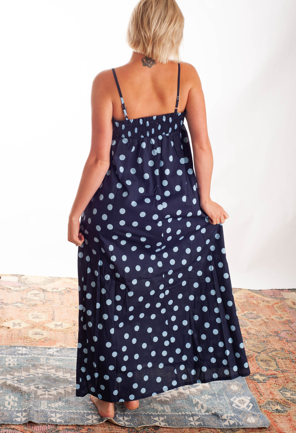 Women wearing a blue polka dot dress against a neutral background.