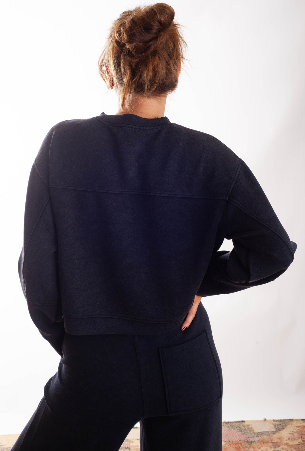 A woman shown from behind wearing a dark navy blue cropped sweatshirt and matching sweatpants against a plain white background.